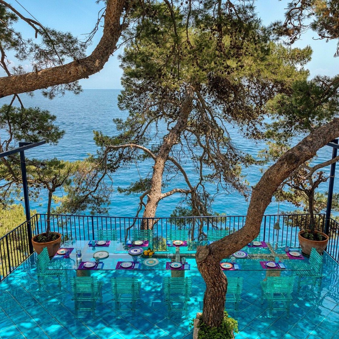   A&rsquo;mare . Die St&uuml;hle der Kollektion sind auf dem blauen Vietri-Keramikboden der von Seekiefern umgebenen Terrasse auf der Klippe getarnt. Sie erzeugen Reflexionen durch Sonnenlicht. 