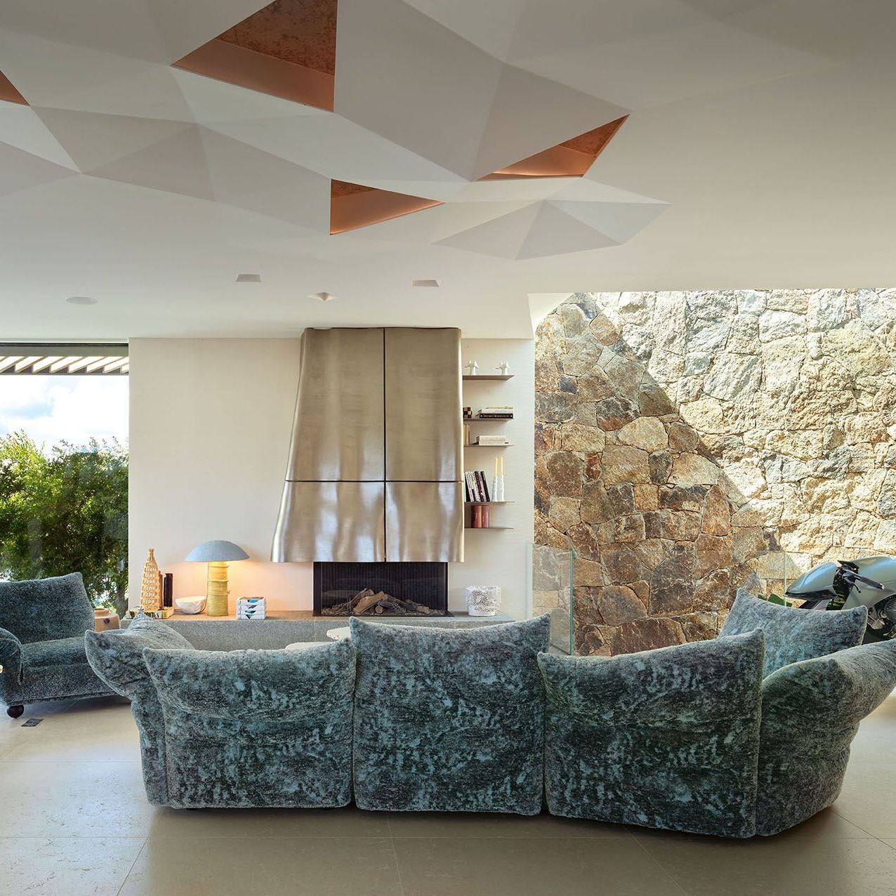  Standard, Standway and Cicladi. The sofa upholstered in Gems Chalcedony and the chaise longue in Gems Botswana Agate in the living area. On the fireplace base, the Gravity Candle Holder by Atelier Fig and the DMT Lamp by Pierre Coddens. On the right, the AMB 001 Motorcycle by Aston Martin & Brough Superior. 